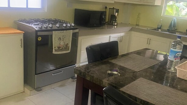 Une cuisine avec des meubles blancs, une cuisinière à gaz, un four à micro-ondes et une table à manger avec des chaises.