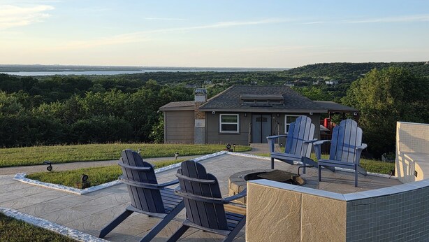 Une terrasse avec des fauteuils Adirondack, un petit bâtiment et une vue sur un lac et une forêt.