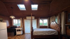 Une chambre dans une cabane en bois, équipée d’un lit, d’un bureau, d’un réfrigérateur et d’une cuisinière.