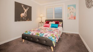 A bedroom with a bed, a nightstand, a lamp, a window with blinds, and two wall art pieces. - Cozy Cottage with Kitchen & Patio (East Tamworth)
