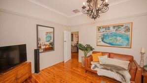 A living room with a TV, a sofa, a chandelier, and a painting. - Cozy Cottage with Kitchen & Patio (East Tamworth)