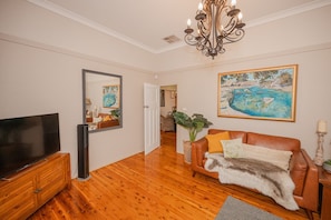 A living room with a TV, a sofa, a chandelier, and a painting. - Cozy Cottage with Kitchen & Patio (East Tamworth)