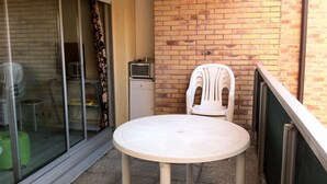 Ein kleiner Balkon mit runder Tisch und einem weißen Kunststoffstuhl, eine Ziegelwand und eine Schiebetür aus Glas.