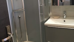 Ein modernes Badezimmer mit einer gläsernen Duschkabine, einem weißen Waschbecken und einem Spiegel.