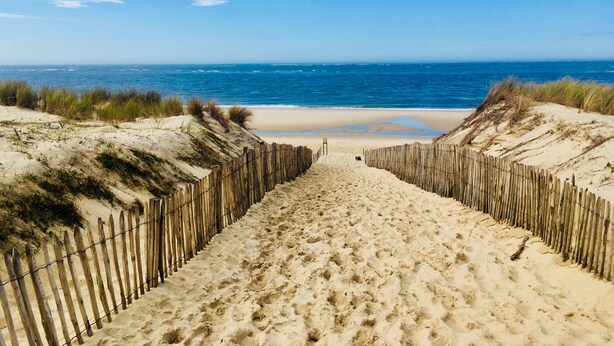 Ein sandiger Strandweg führt zum Meer, gesäumt von Holzzaunen.