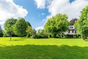 A well-maintained lawn, a large tree, and a building with a sloped roof. - Charming Normandy cottage with large garden, sheltered from the wind and 10' from the sea (Luneray)