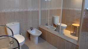 Een badkamer met een toilet, een bidet en een grote spiegel.
