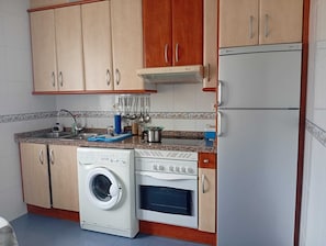 Eine kompakte Küche mit Waschmaschine, Backofen und kleinem Kühlschrank.