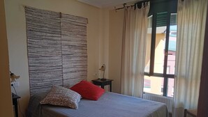 Een slaapkamer met een bed, nachtkastje, lamp en een raam met gordijnen.
