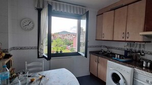 Een kleine keuken met een wasmachine, een spoelbak en een raam met uitzicht op gebouwen.