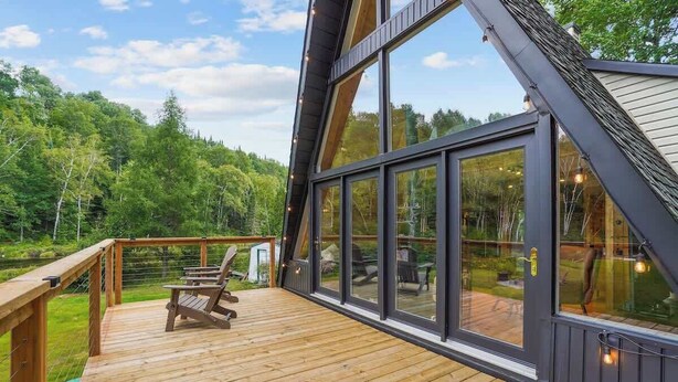 Une terrasse en bois avec une chaise, de grandes fenêtres et une vue sur une forêt.