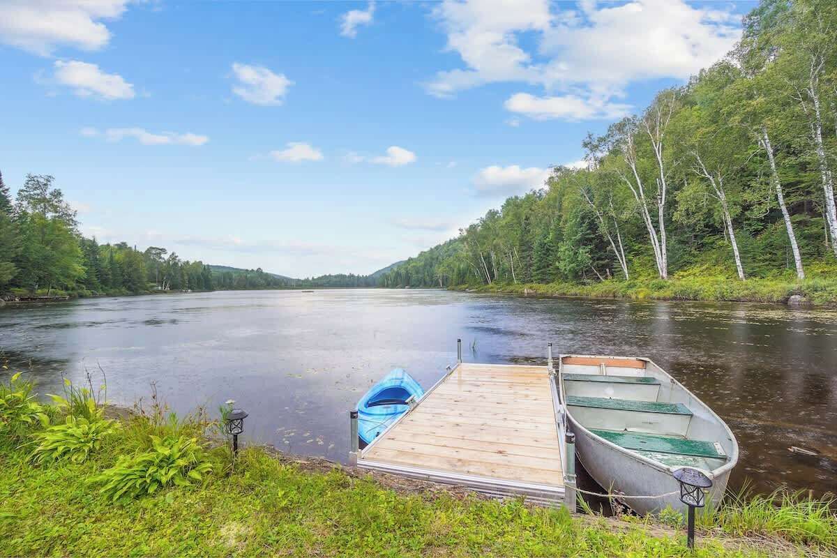 A calm river with boats docked at a wooden pier, surrounded by lush greenery and trees.