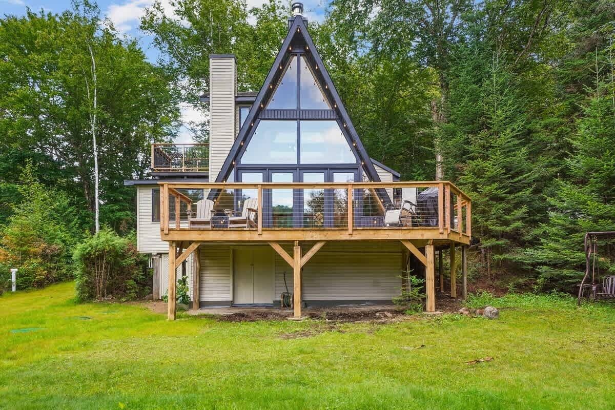 A house with a prominent triangular roof, a wooden deck with seating, and a garage.