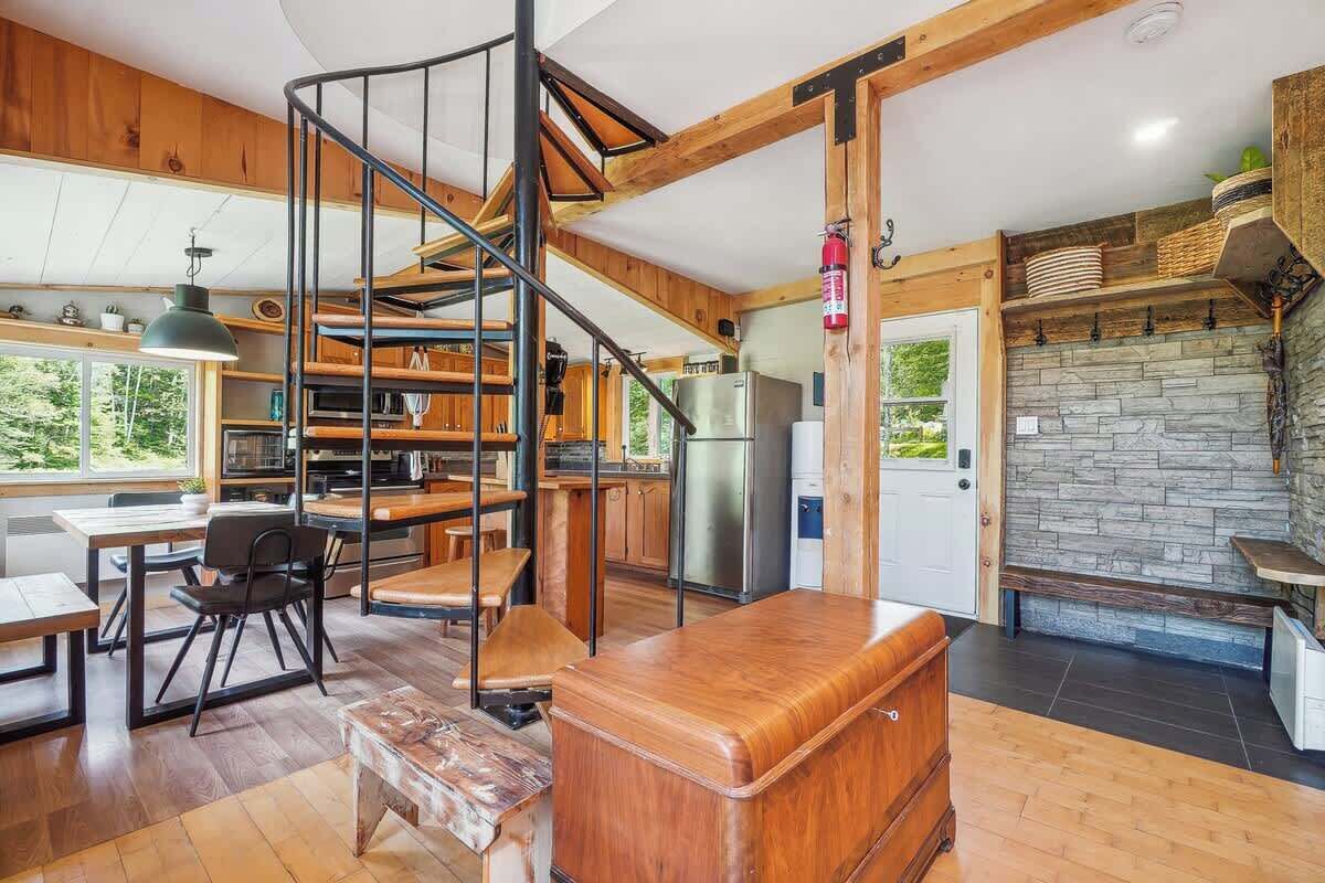 A modern kitchen with a wooden staircase, a dining area, and a stone fireplace.