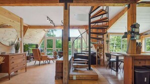 Un loft spacieux avec un intérieur en bois, un escalier en colimaçon et de grandes fenêtres offrant une vue sur la verdure.
