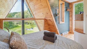 Une chambre avec une grande fenêtre, un lit recouvert d’une literie à motifs et une vue sur la verdure.
