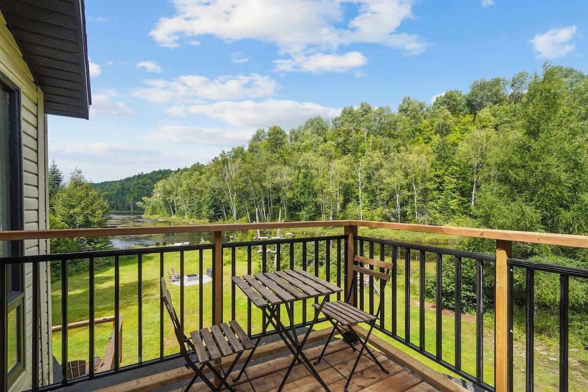 Un balcon avec une table et des chaises en bois, donnant sur un paysage verdoyant et une rivière.