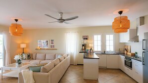 Ein modernes Wohnzimmer mit Sofa, Couchtisch und einer Küche mit Kochinsel, weißen Schränken und einem Deckenventilator.