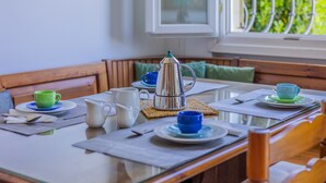 Et morgenbord dækket med kopper, kande og tekedel, med udsigt til grønt gennem et vindue.