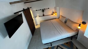 Un dormitorio con cama, lámparas de noche, una estantería con una planta y una puerta corredera.