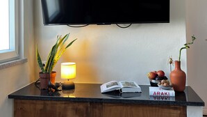 Un televisor de pantalla plana montado en una pared sobre una encimera de madera con una planta en maceta, una lámpara y un frutero.