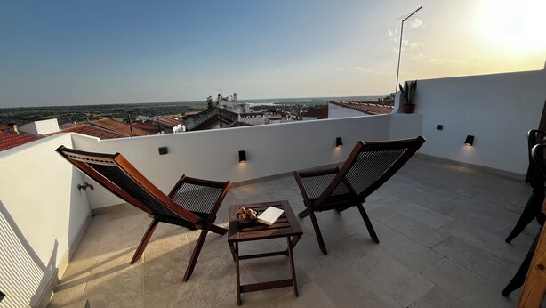 Una terraza en la azotea con dos sillas de madera, una mesa pequeña y vistas a la ciudad.