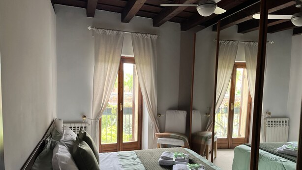 A bedroom with a bed, a chair, a radiator, and a window with curtains. - Adige View Suite (Verona)