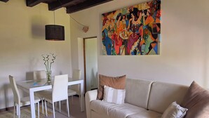 A living room with a white sofa, a dining table with chairs, a vase with plants, and a colorful abstract painting on the wall. - Adige View Suite (Verona)