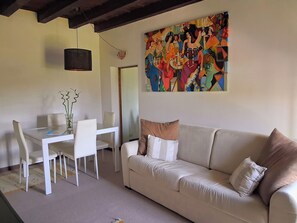 A living room with a white sofa, a dining table with chairs, a vase with plants, and a colorful abstract painting on the wall. - Adige View Suite (Verona)