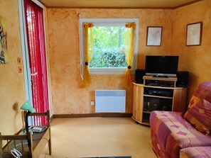 A room with a television, a heater, a window with curtains, a chair, and a bed. - Wooden mobile home on a residential leisure park access to the leisure area (La teste de buch)