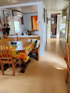 A dining area with a table covered in a colorful tablecloth, wooden chairs, and a ceiling fan. - Wooden mobile home on a residential leisure park access to the leisure area (La teste de buch)