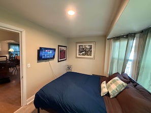 Un dormitorio con cama, televisor montado en la pared y un cuadro enmarcado.