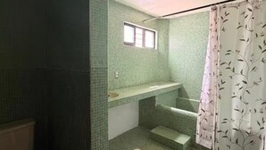 Une salle de bain avec des carreaux de mosaïque verts, une fenêtre, une douche avec un rideau à motifs floraux et des toilettes.