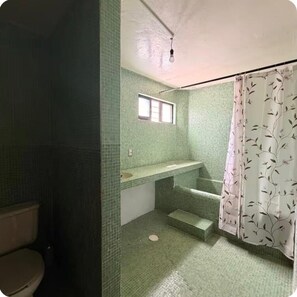 A bathroom with green mosaic tiles, a window, a shower with a floral curtain, and a toilet. - Casa rústica en Jiutepec con alberca, jardín y asador ideal para descansar. (Jiutepec)