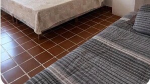 Une chambre avec un lit simple, une couvre-lit à motifs, une lampe de chevet, une petite table avec un téléphone et une fenêtre avec des rideaux.