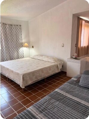 A single-bed room with a patterned bedspread, a bedside lamp, a small table with a phone, and a window with curtains. - Casa rústica en Jiutepec con alberca, jardín y asador ideal para descansar. (Jiutepec)