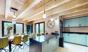 A modern kitchen with a large island, green cabinets, and a wall clock. - Cosy chalet with jacuzzi for 11 (Bonnevaux)