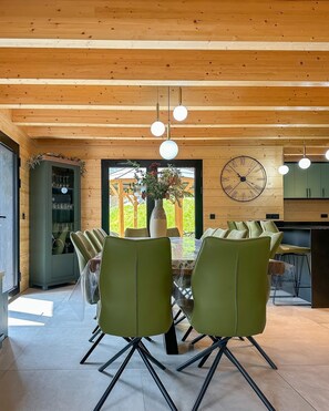 A dining area with a wooden ceiling, a large wall clock, and a view through a glass door. - Cosy chalet with jacuzzi for 11 (Bonnevaux)
