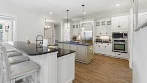 Una cucina moderna con mobili bianchi, un'isola centrale, elettrodomestici in acciaio inossidabile e un'area con bancone.