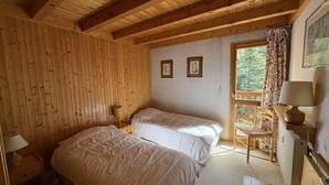 Una habitación con dos camas, paredes de madera, una ventana con vistas y una silla junto a la ventana.