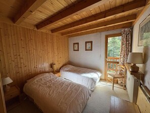 Ein Zimmer mit zwei Betten, Holzwänden, einem Fenster mit Blick und einem Stuhl am Fenster.
