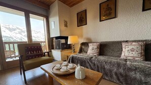 Una habitación acogedora con una mesa de madera dispuesta para el té, un sofá con cojines decorativos y vistas a montañas a través de amplios ventanales.