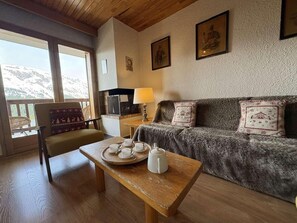 Ein gemütliches Zimmer mit einem Holztisch, gedecktem für Tee, einer Couch mit dekorativen Kissen und Blick auf Berge durch große Fenster.