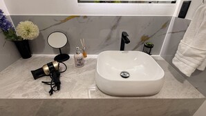 Un bagno con un lavandino bianco, uno specchio, un asciugacapelli e una pianta in vaso.