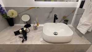 Ein Badezimmer mit einem weißen Waschbecken, einem Spiegel, einem Fön und einer Topfpflanze.