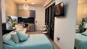 Un ambiente abitativo compatto con un letto, angolo cottura e TV a parete.