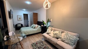 Ein gemütlicher, kleiner Wohnraum mit Bett, Sofa, Tisch und einem Topfpflanzen.