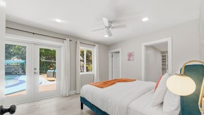 Et soveværelse med seng, ventilator, udsigt til et pool og en dør, der fører til en balkon.
