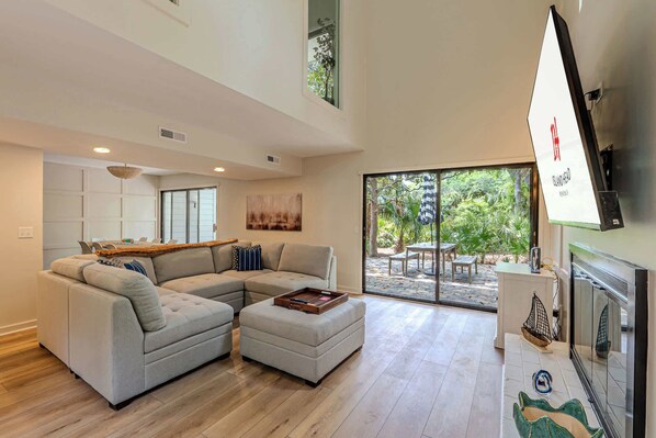 Una sala moderna con un sofá modular, un pequeño taburete y un amplio ventanal corredera que da a un patio exterior.