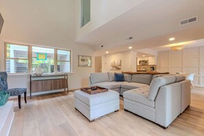 Amplio salón con un sofá seccional, una mesa de centro de madera y vistas a través de grandes ventanales.